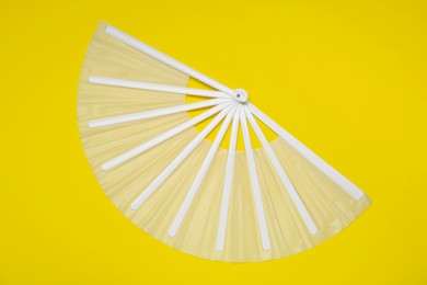 Photo of White hand fan on yellow background, top view