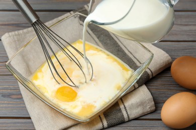 Photo of Adding milk to whisked eggs at wooden table, closeup