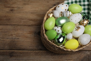 Photo of Many beautifully decorated Easter eggs in wicker basket on wooden table, above view. Space for text