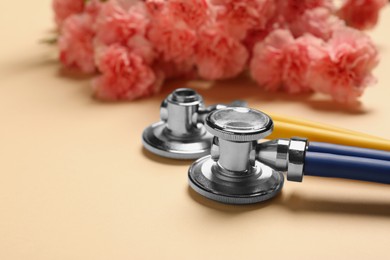 Photo of Stethoscopes and beautiful flowers on beige background, closeup. Happy Doctor's Day