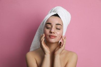 Woman applying pomegranate face mask on pink background