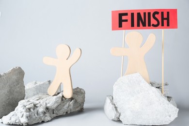 Photo of Competition concept. Wooden human figures on stones and red sign with word Finish against grey background