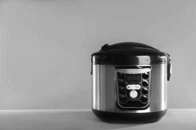 Photo of Modern powerful multi cooker on table against grey background. Space for text