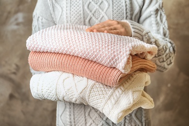 Photo of Young woman holding stack of warm knitted clothes, closeup