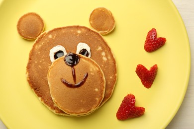 Creative serving for kids. Plate with strawberries, cute bear made of pancakes on table, top view