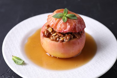 Photo of Tasty baked apple with nuts, honey and mint on gray table, closeup