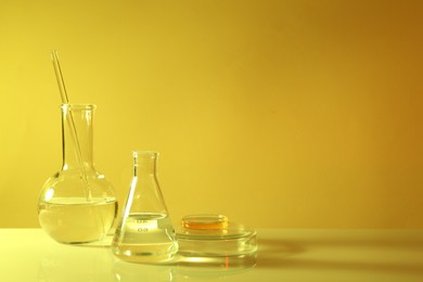 Photo of Laboratory analysis. Different glassware on table against yellow background, space for text