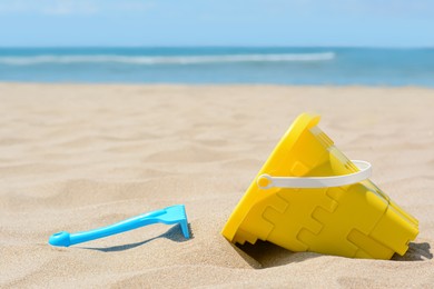 Photo of Plastic bucket and rake on sand near sea, space for text. Beach toys