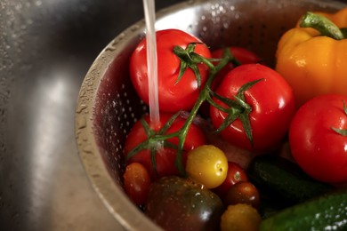 Photo of Washing different vegetables with tap water in metal colander inside sink, closeup