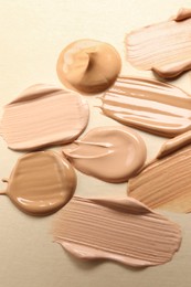 Photo of Samples of skin foundation on beige background, closeup
