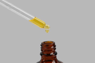 Photo of Dripping tincture from pipette into bottle on white background