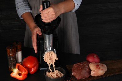 Woman making chicken mince with electric meat grinder at black table, closeup