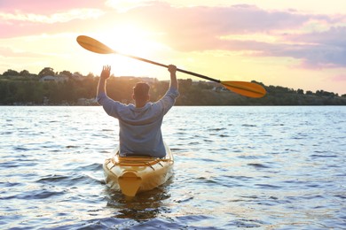 Photo of Man kayaking on river at sunset, back view. Summer activity
