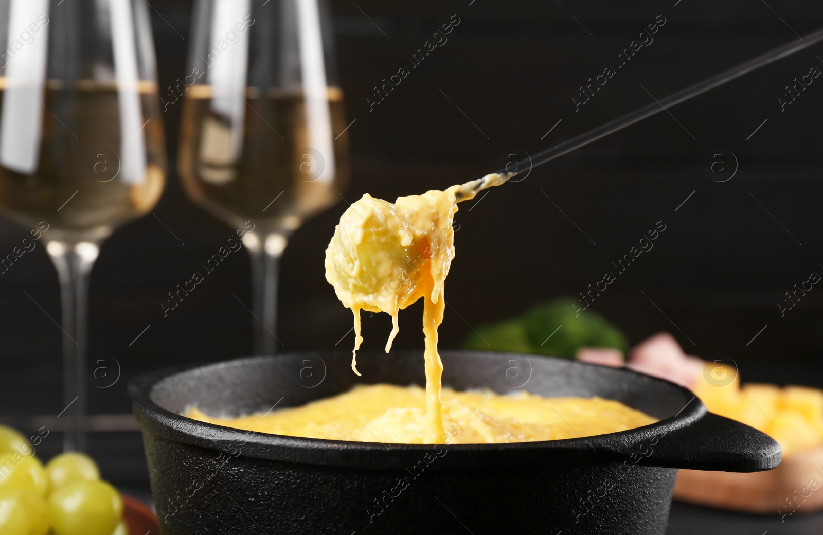 Photo of Dipping grape into fondue pot with melted cheese on table, closeup