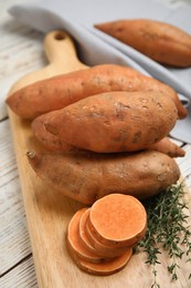 Photo of Wooden board with thyme and sweet potatoes on table