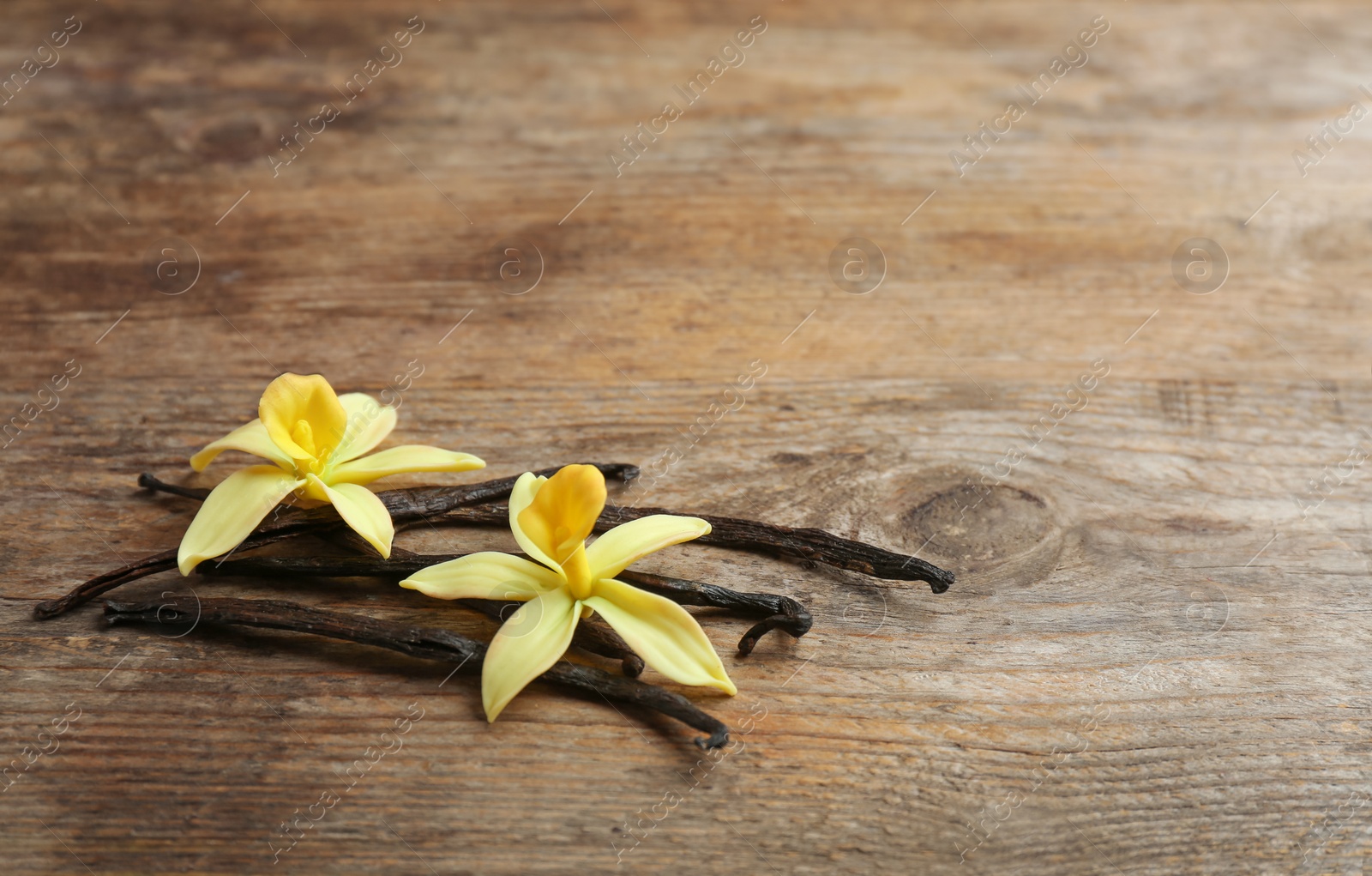 Photo of Vanilla sticks and flowers on wooden background. Space for text