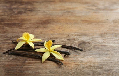 Vanilla sticks and flowers on wooden background. Space for text