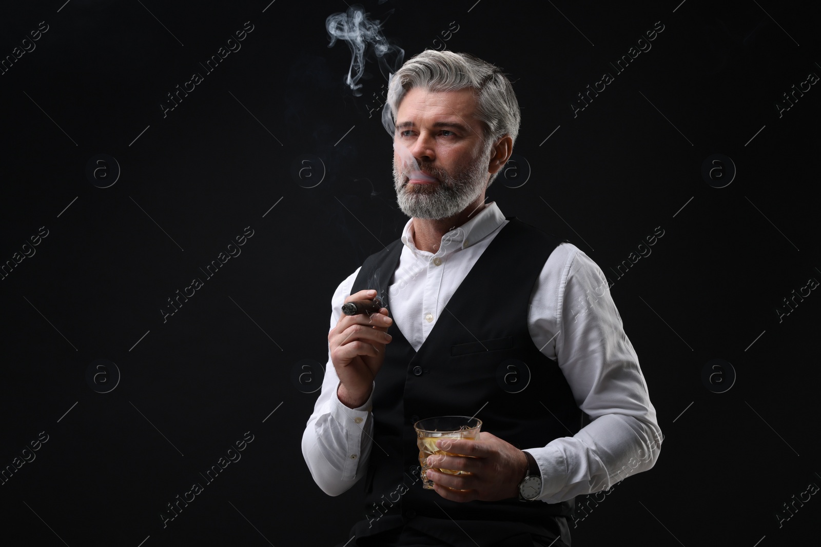 Photo of Bearded man with glass of whiskey smoking cigar against black background. Space for text