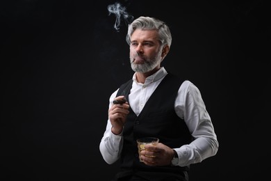 Photo of Bearded man with glass of whiskey smoking cigar against black background. Space for text