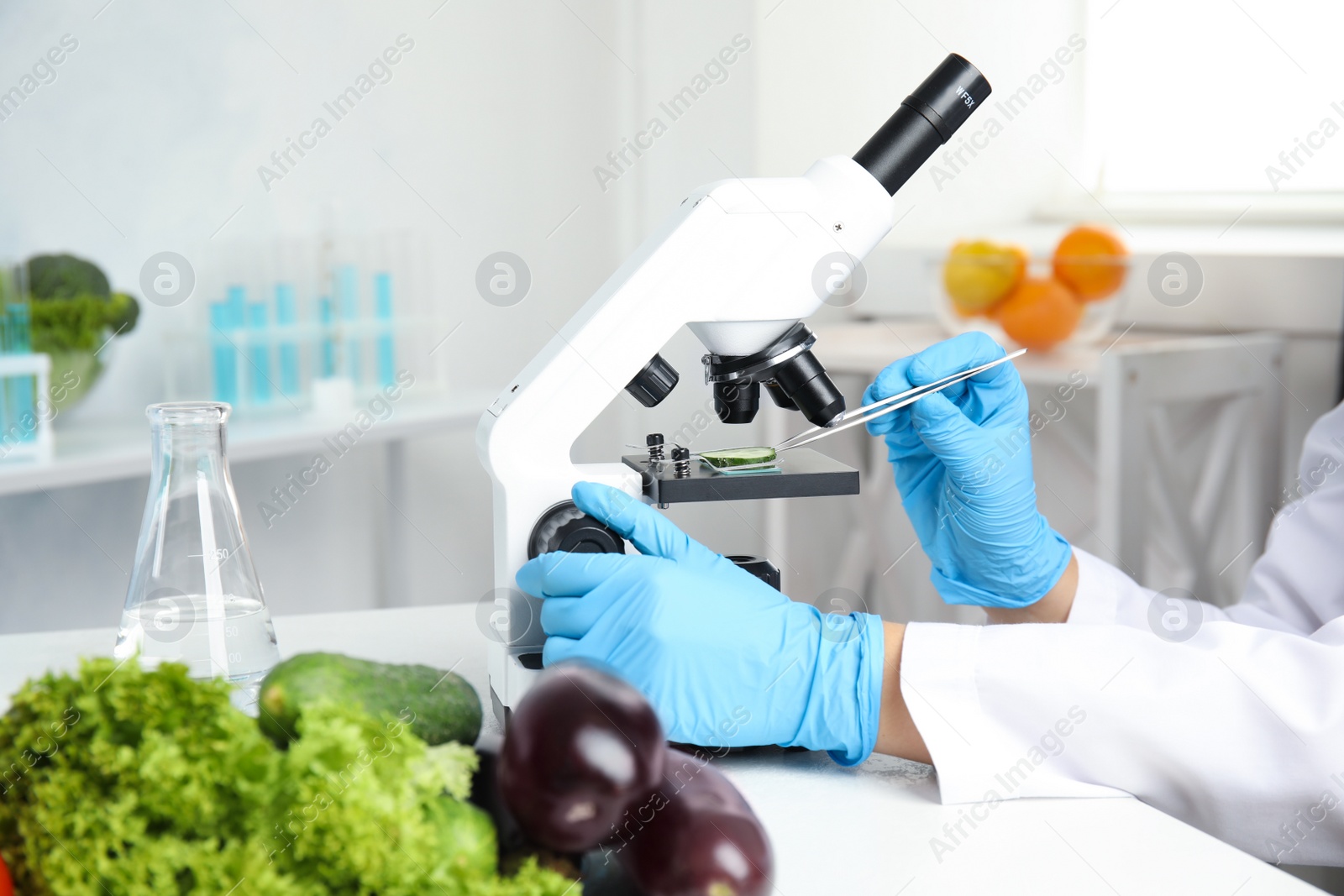 Photo of Scientist inspecting slice of cucumber with microscope in laboratory, closeup. Poison detection