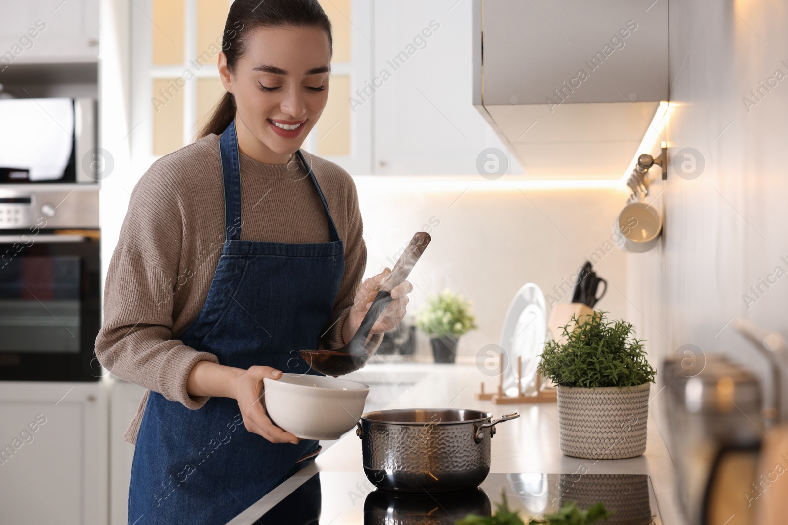 Photo of Smiling woman pouring tasty soup into bowl at countertop in kitchen