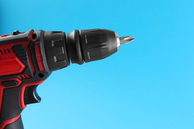 Modern electric screwdriver on light blue background, closeup. Space for text