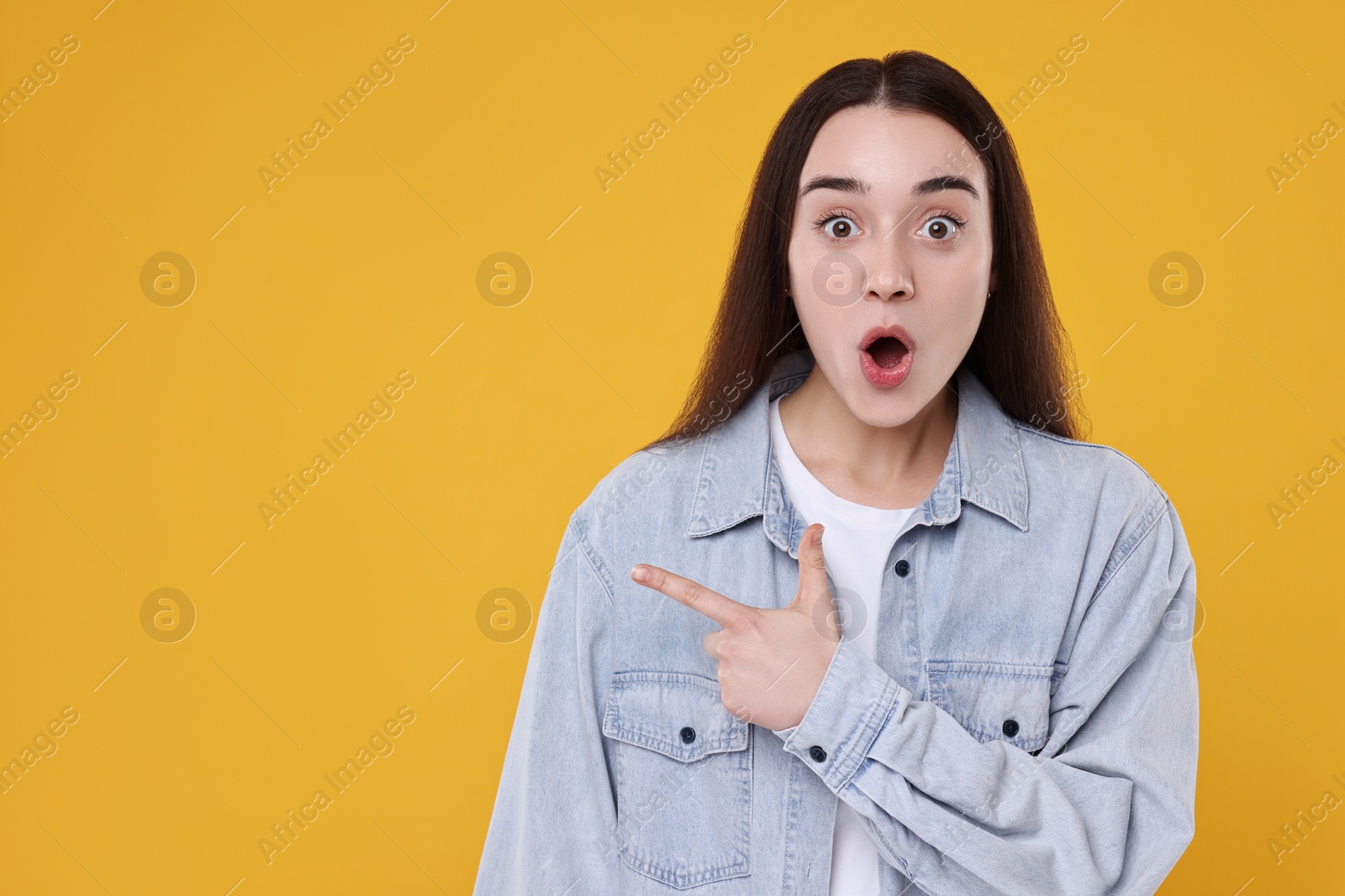 Photo of Portrait of surprised woman pointing at something on yellow background. Space for text