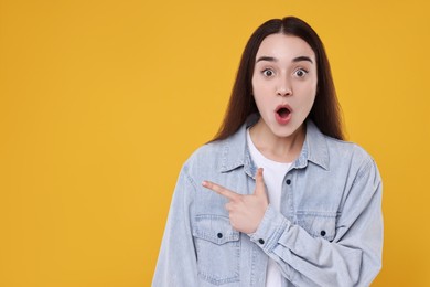 Portrait of surprised woman pointing at something on yellow background. Space for text