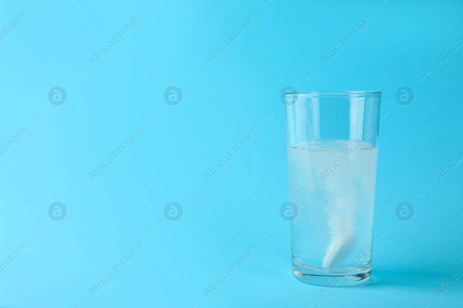 Photo of Glass of water with effervescent tablet on light blue background, space for text