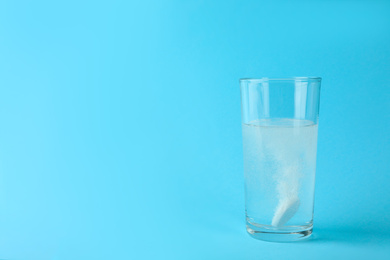 Photo of Glass of water with effervescent tablet on light blue background, space for text