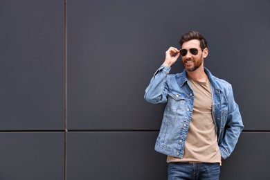 Handsome bearded man with sunglasses leaning to grey wall outdoors. Space for text