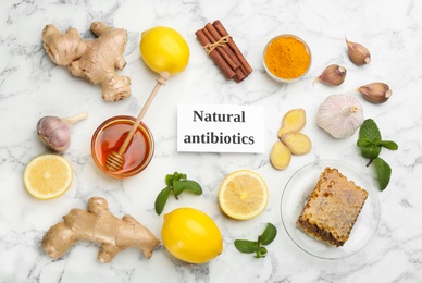 Different fresh products and card with phrase Natural Antibiotic on white marble table, flat lay