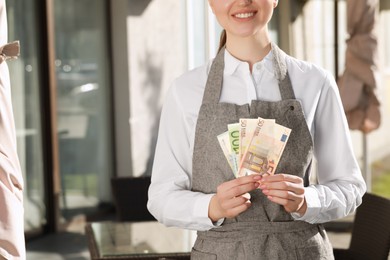 Photo of Happy waitress holding payment for order and tips at outdoor cafe, closeup
