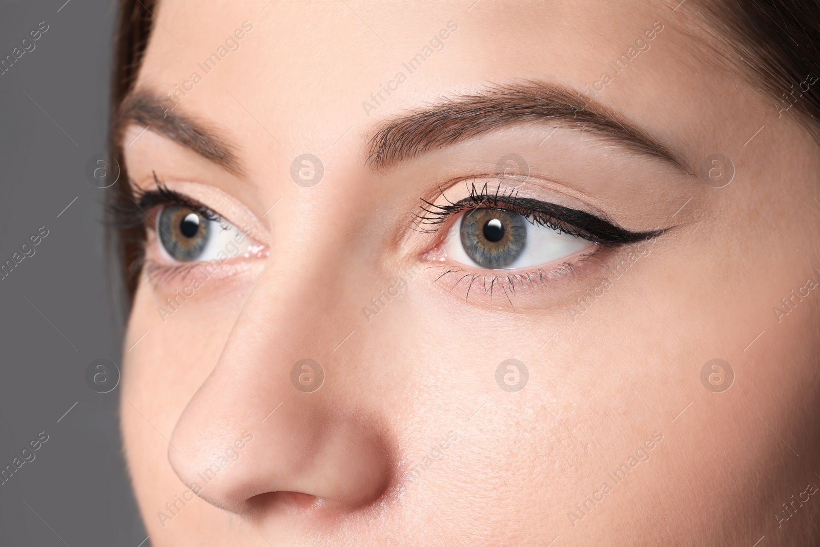 Photo of Beautiful woman with black eyeliner on grey background, closeup