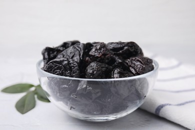 Sweet dried prunes in bowl on light table, closeup