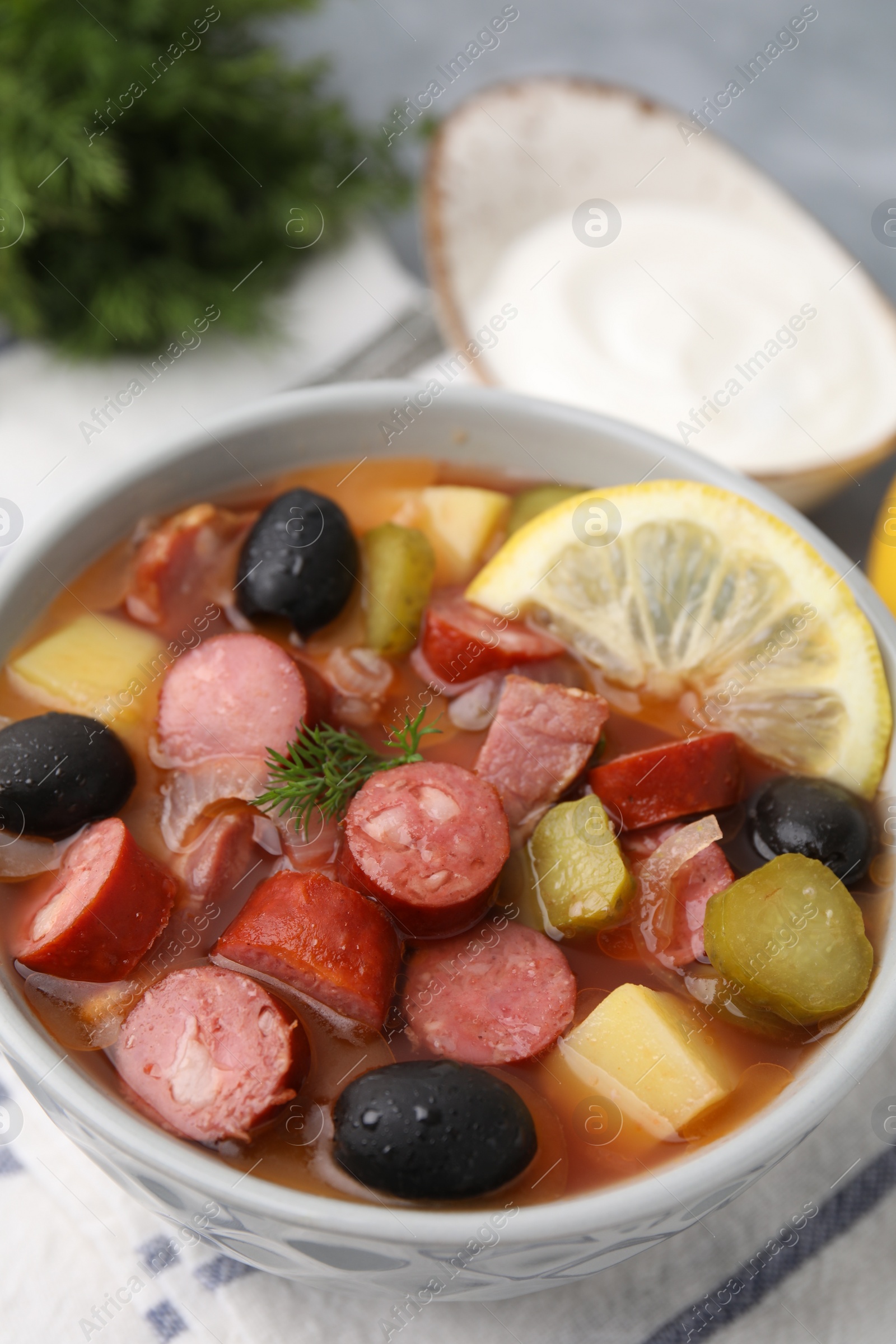 Photo of Meat solyanka soup with thin dry smoked sausages in bowl on table, closeup