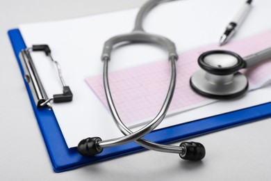 Photo of Stethoscope, clipboard and cardiogram paper on white background, closeup