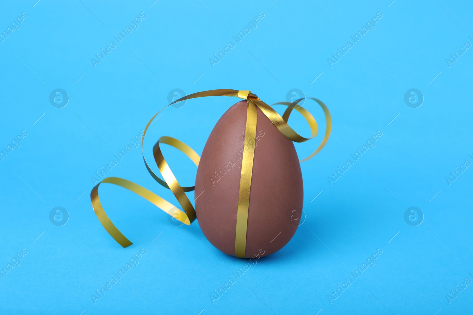 Photo of Delicious chocolate egg with silver ribbon on light blue background, closeup