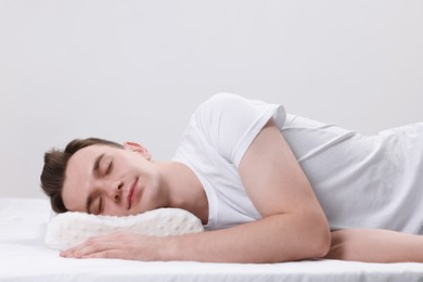 Man sleeping on orthopedic pillow against light grey background