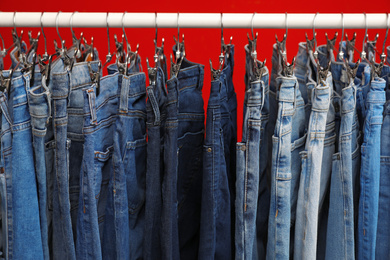 Photo of Rack with stylish jeans on red background, closeup