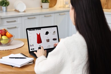 Woman with laptop shopping online at wooden table in kitchen, closeup