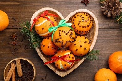 Pomander balls made of tangerines with cloves and fir branches on wooden table, flat lay