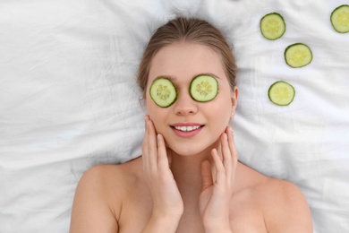 Beautiful woman with cucumber slices on white fabric, above view. Organic face mask