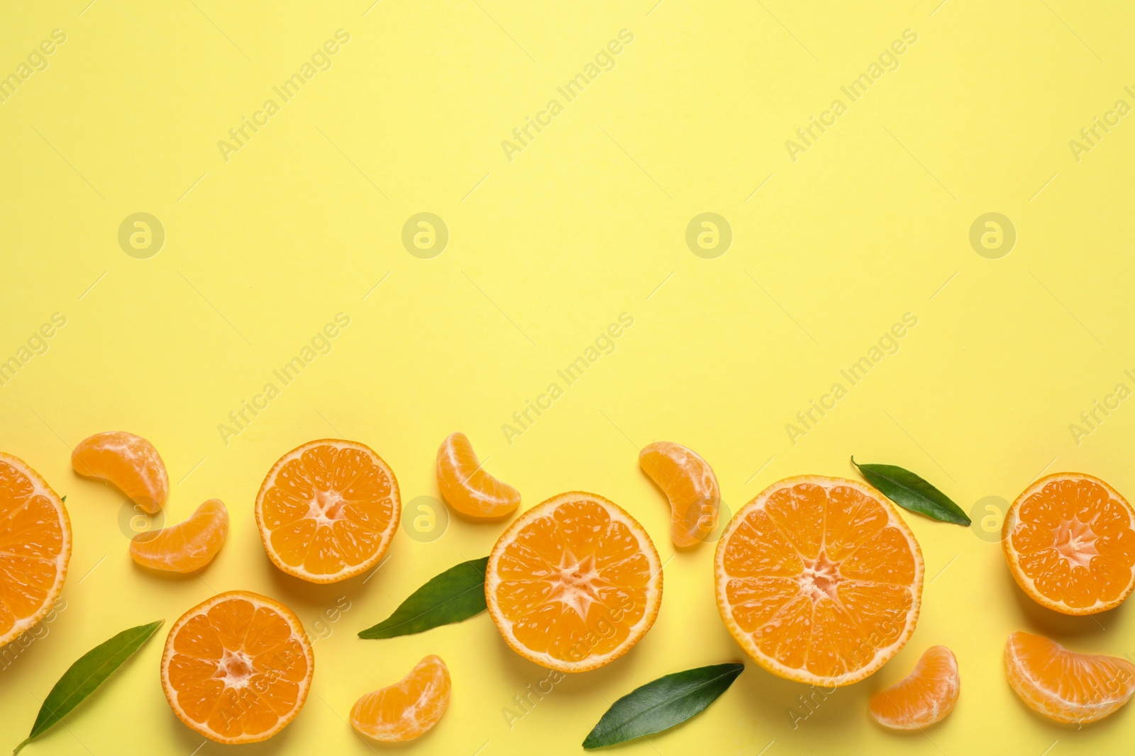 Photo of Flat lay composition with fresh ripe tangerines and leaves on light yellow background, space for text. Citrus fruit