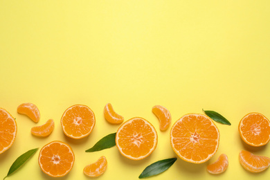 Flat lay composition with fresh ripe tangerines and leaves on light yellow background, space for text. Citrus fruit