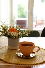 Cup of delicious chamomile tea and fresh flowers on wooden table in room