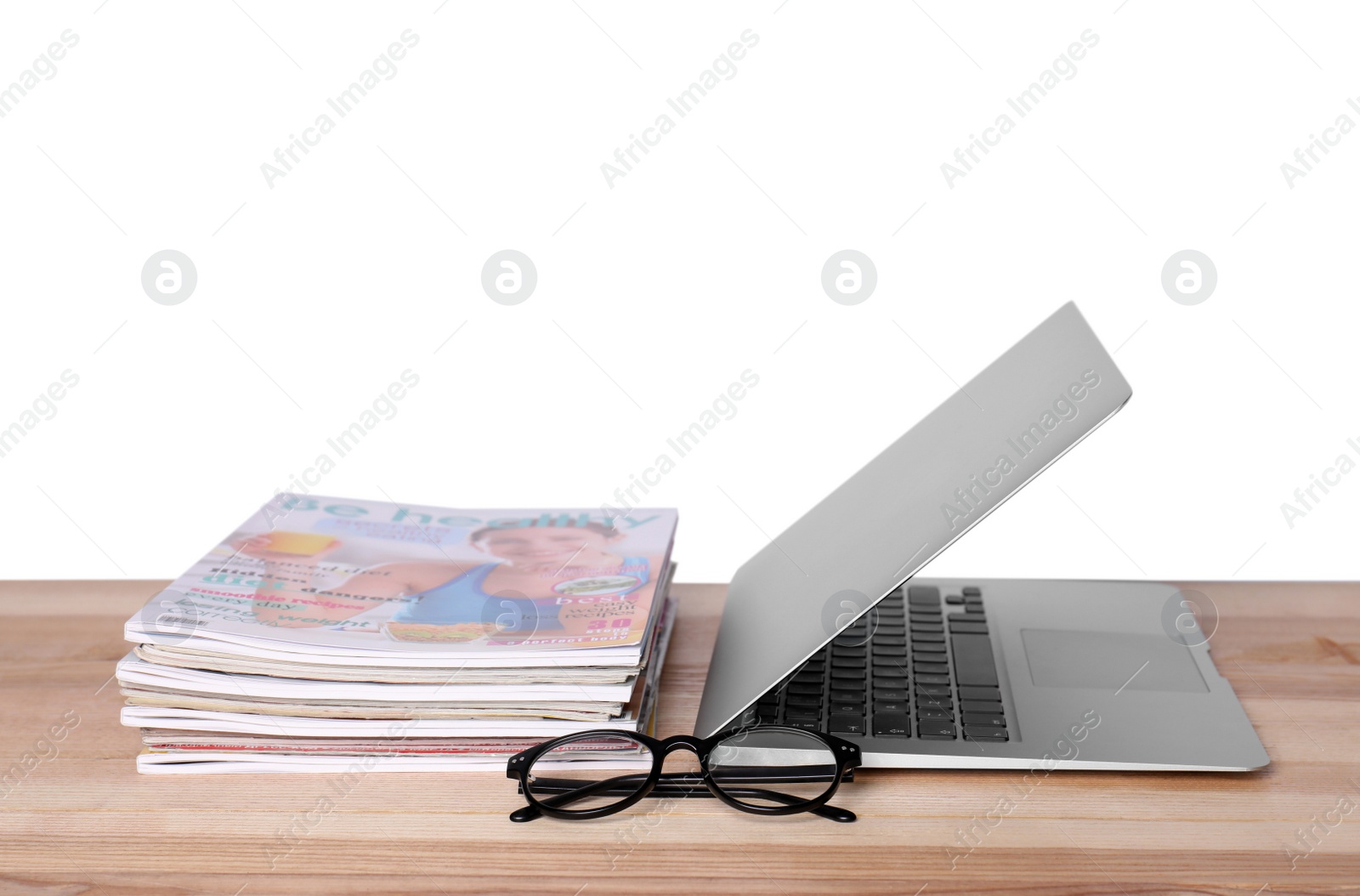 Photo of Laptop, glasses and stack of magazines on wooden table