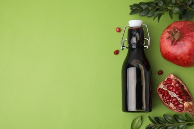 Photo of Tasty pomegranate sauce in bottle, branches and cut fruit on green table, flat lay. Space for text