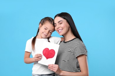 Photo of Happy woman with her cute daughter and handmade greeting card on light blue background. Mother's day celebration