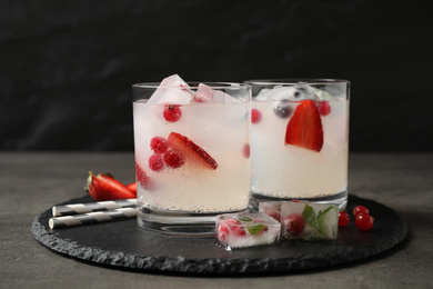 Glasses of refreshing drink with ice cubes and berries on grey table